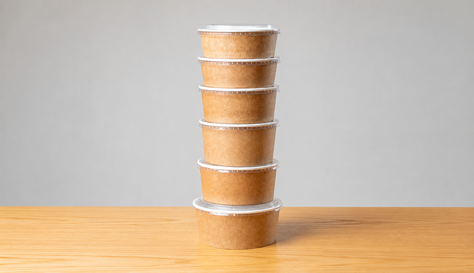 Pilha de bowls de papel Kraft com tampas transparentes sobre superfície de madeira